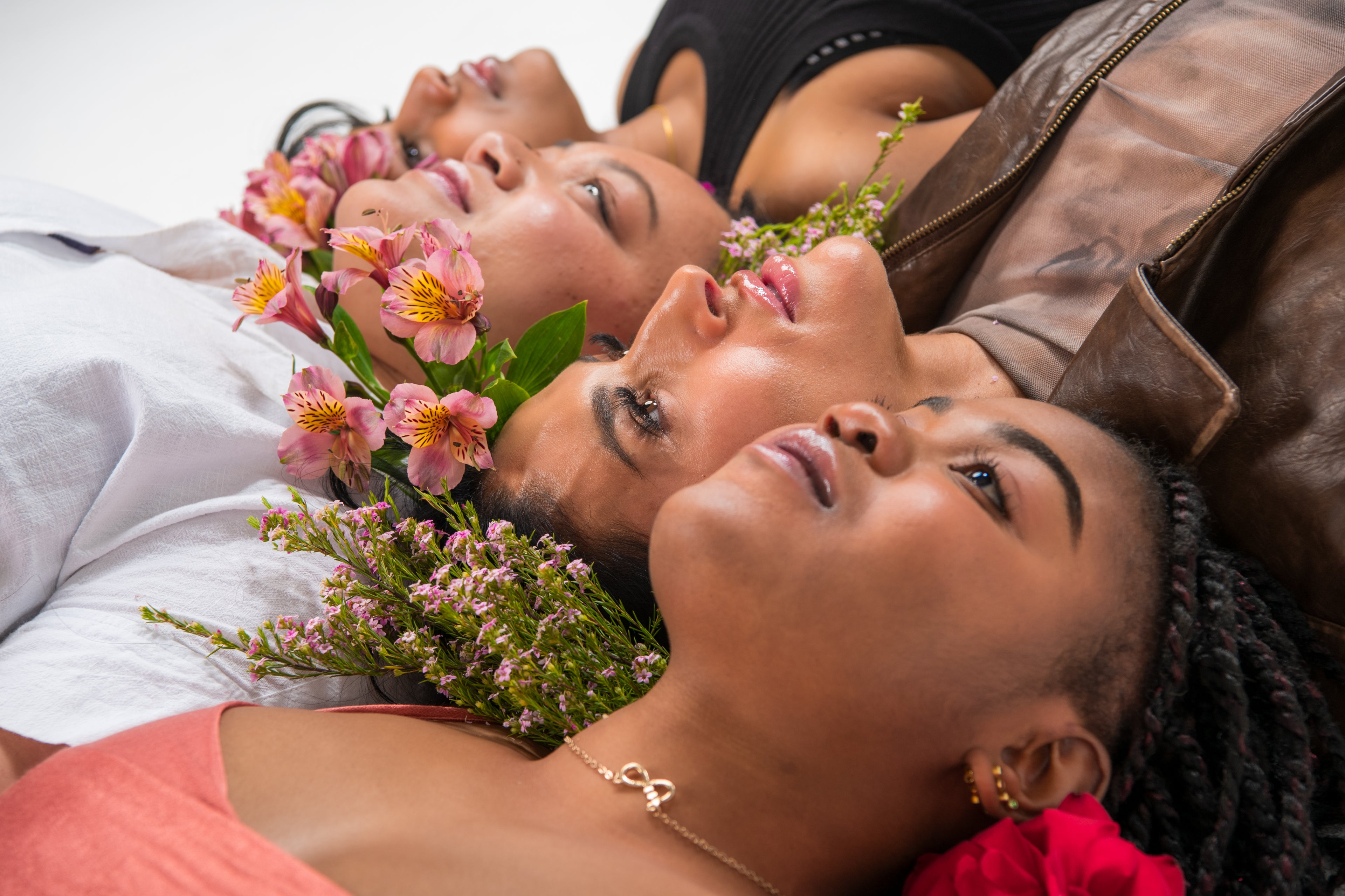 Three women lying down with flowers in their hair, wearing white and pink clothing.