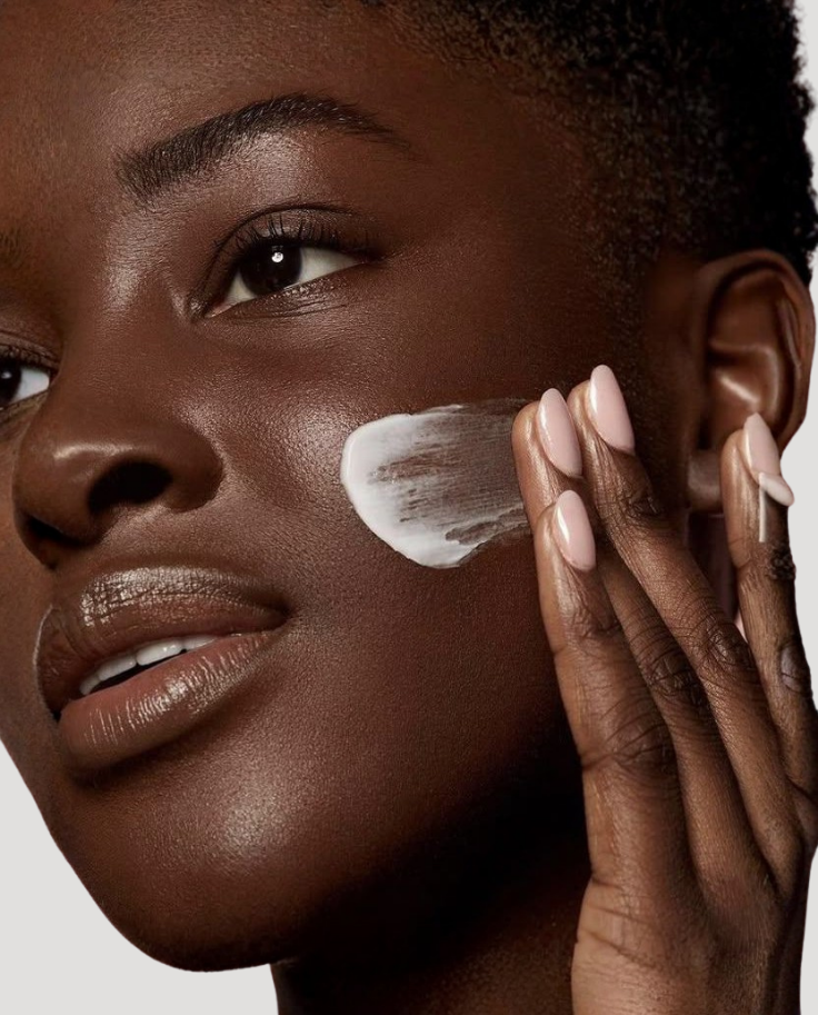 Woman applying cream to her face with a neutral background
