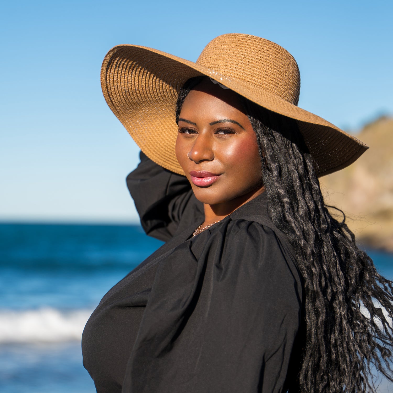 Woman wearing a wide-brimmed hat on a beach with ocean and sky in the background