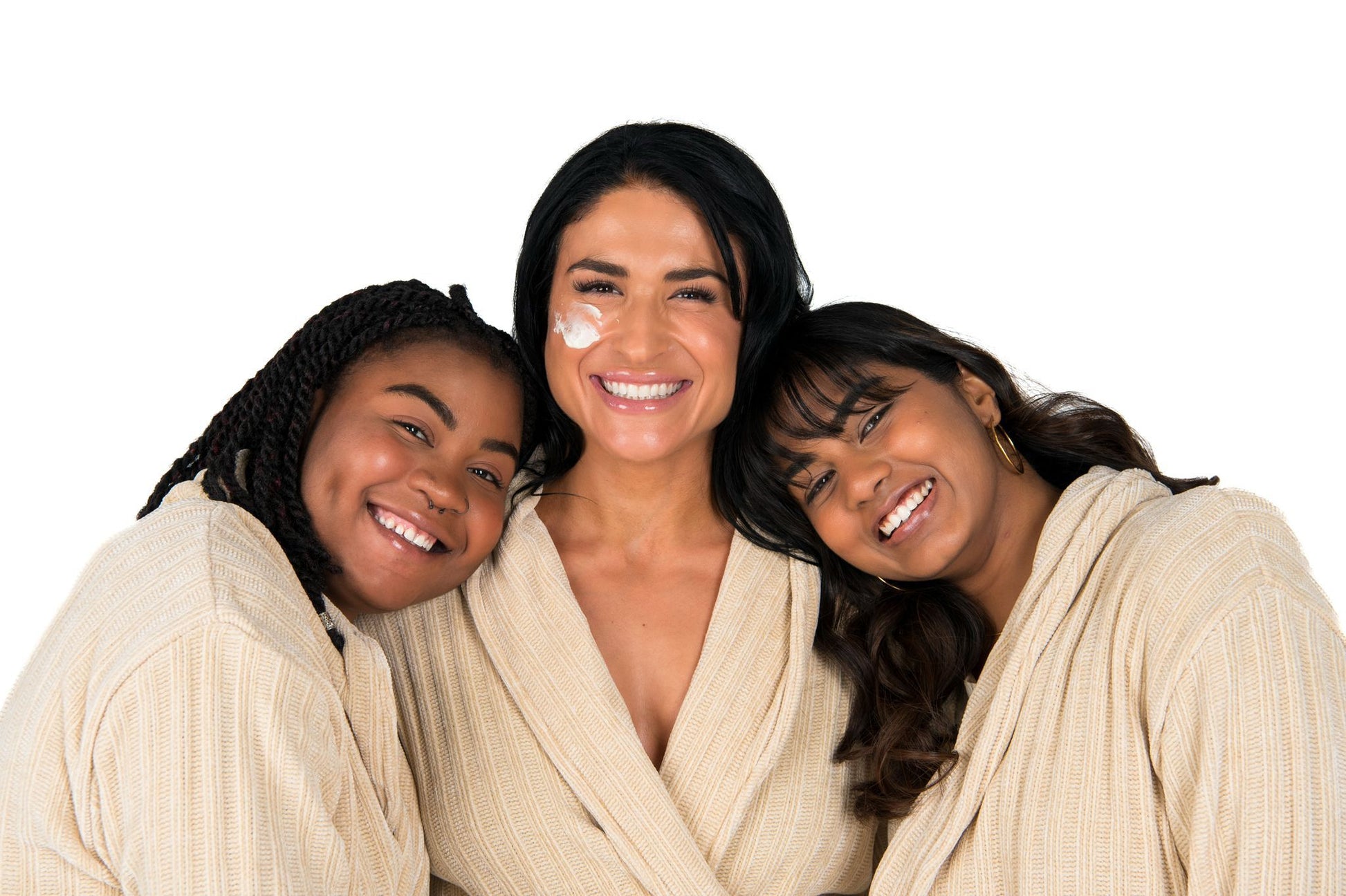 Three women wearing beige robes against a white background
