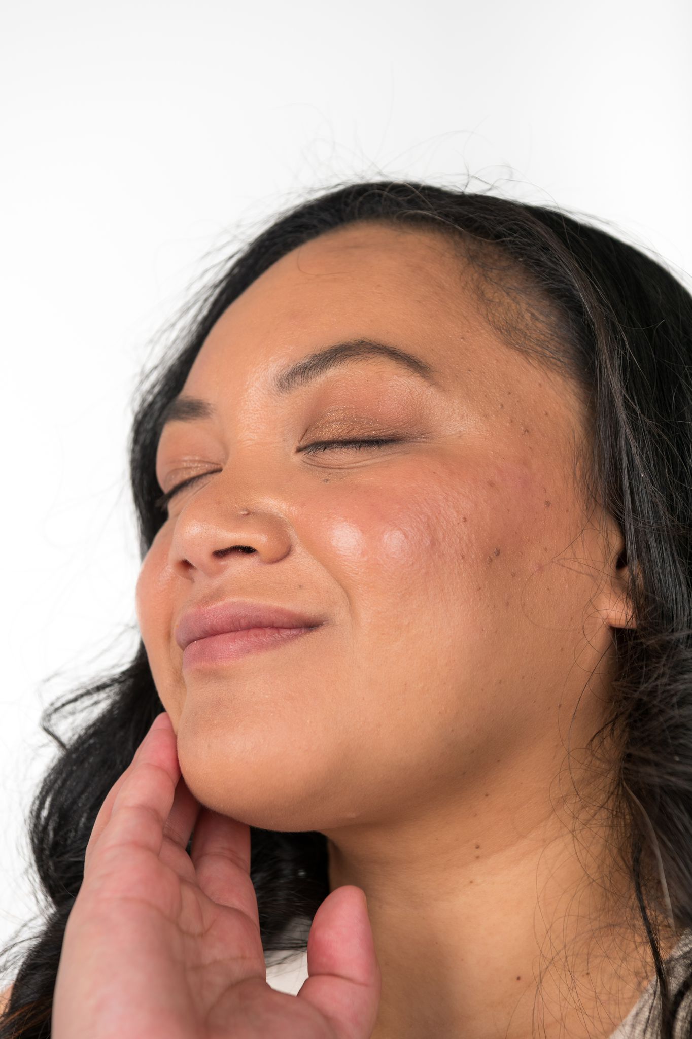 Close-up of a person with their eyes closed, touching their neck against a white background