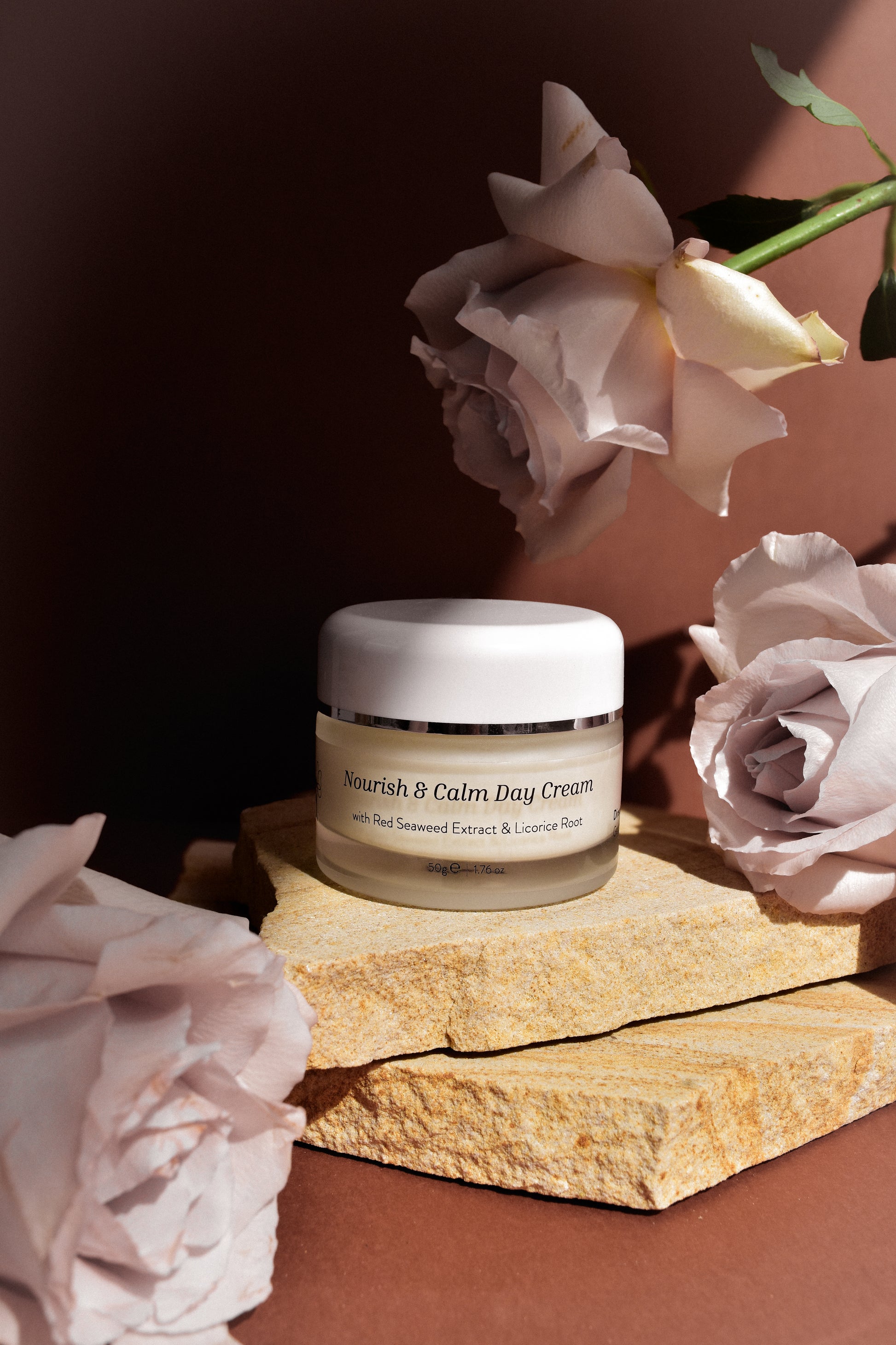 Jar of Nourish & Calm Day Cream with pink roses on a stone surface