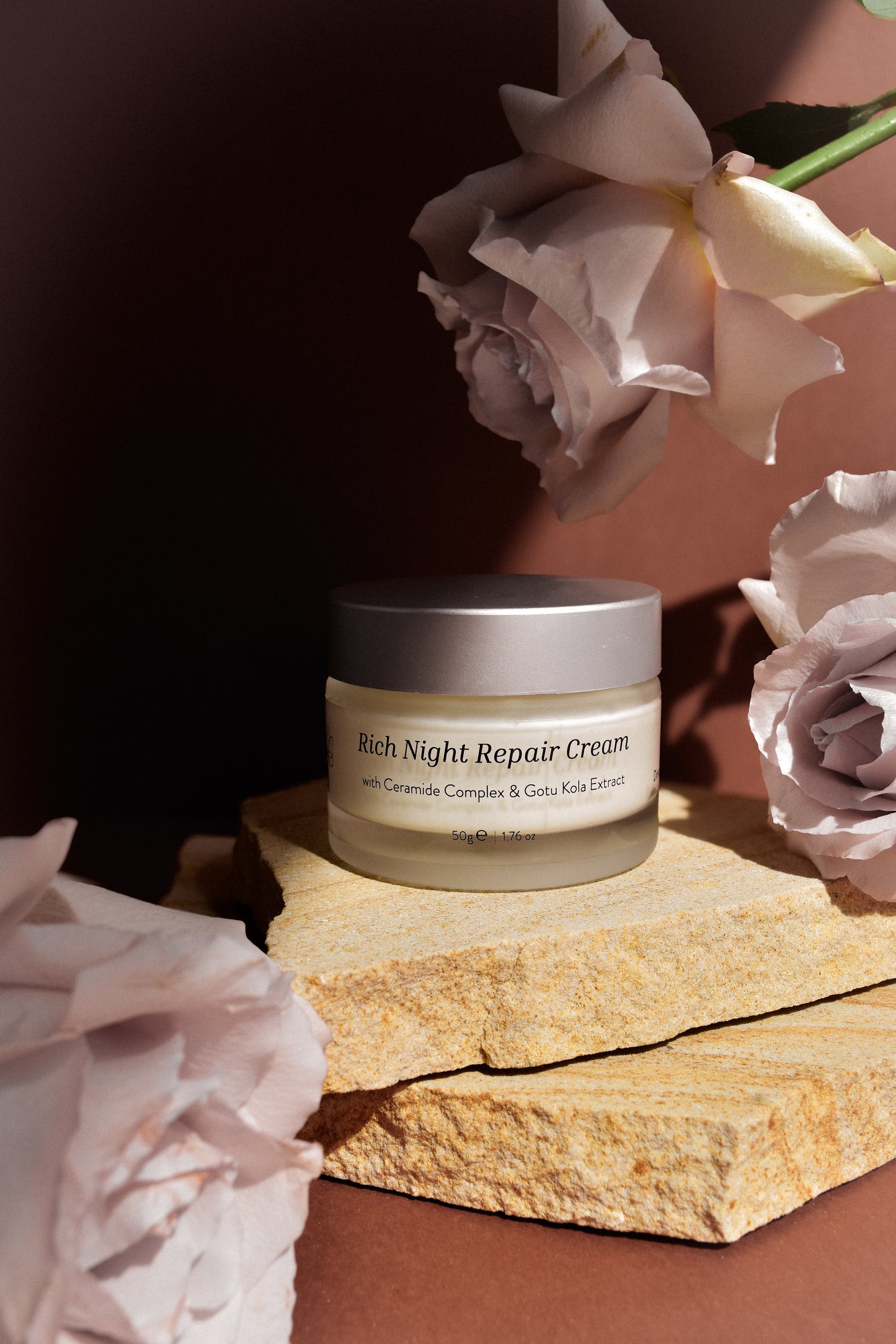 Jar of Rich Night Repair Cream with flowers on a stone surface